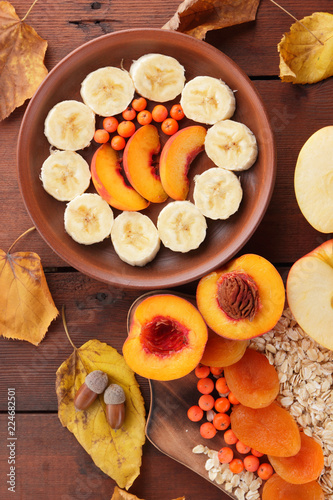 Oatmeal with different fruits and honey. Oat flakes with milk and dried apricots on wooden background. Healthy food for vegan. Dry oats with berries of mountain ash and green mint. Autumn pattern