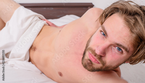 He waits for you. Guy sexy macho lay white bedclothes. Playful mood concept. Pleasant relax concept. Man feel satisfied after pleasant night dream. Man unshaven handsome sexy torso relaxing bed