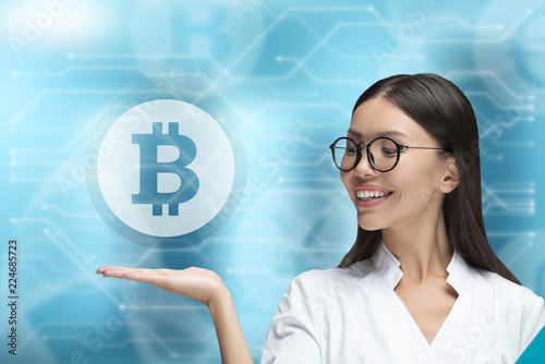 Medical and currency mixed media concept. A woman doctor is raising her hand to hold a Bitcoin money symbol. 