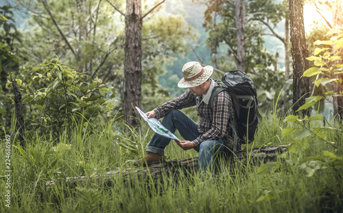 male hiker with backpack sitting and look at map and checking in the forest