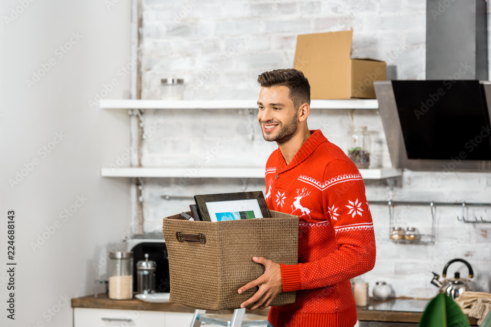 happy young man carrying box in kitchen during relocation in new home happy young man carrying box in kitchen during relocation in new home