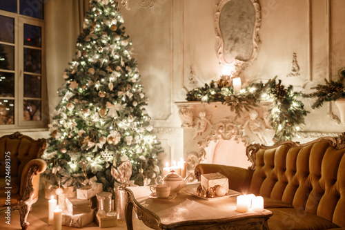 Christmas tree, garlands, candles,lanterns, gifts in the evening. classical interior of a white room with a decorated fireplace, sofa,