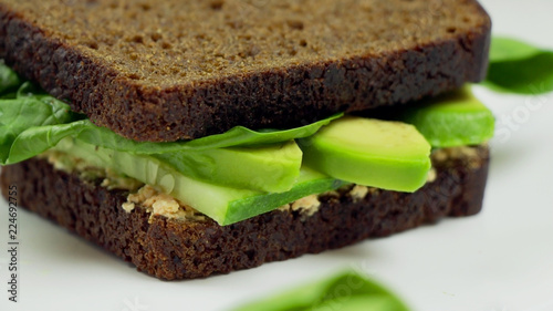 Avocado sandwich on dark rye bread made with fresh sliced avocado, spinach and cream cheese