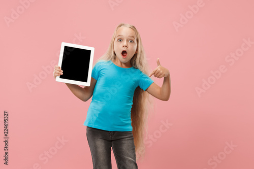 Little funny girl with tablet on pink studio background. She showing something and pointing at screen.