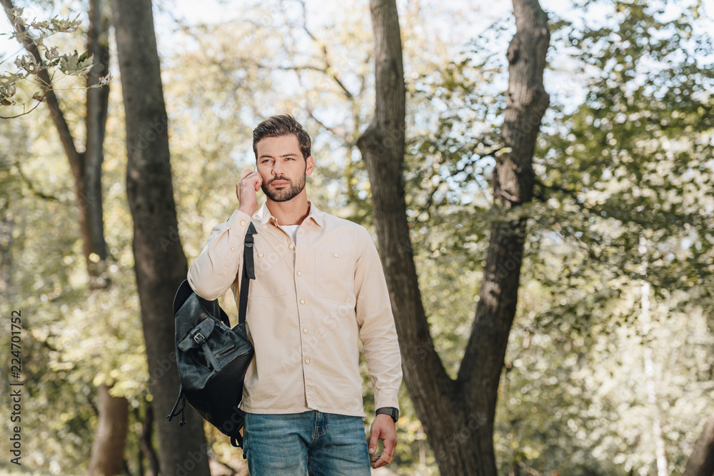 portrait of young man with backpack talking on smartphone in park portrait of young man with backpack talking on smartphone in park