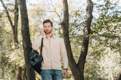portrait of young man with backpack talking on smartphone in park