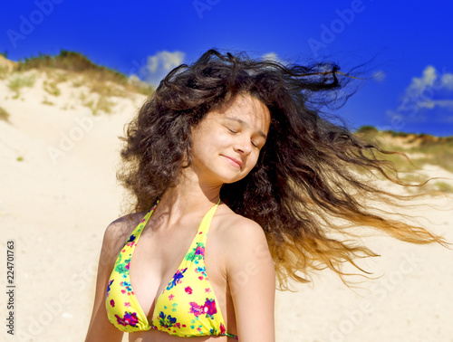 Outdoor fashion photo of beautiful happy woman at sea. Beach travel. Summer vibes. stylish girl in a yellow swimsuit standing with flying hair from the wind on the beach