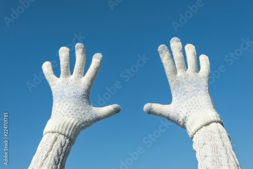 Female hands in the winter knitted mittens on the clear blue sky background. Concept