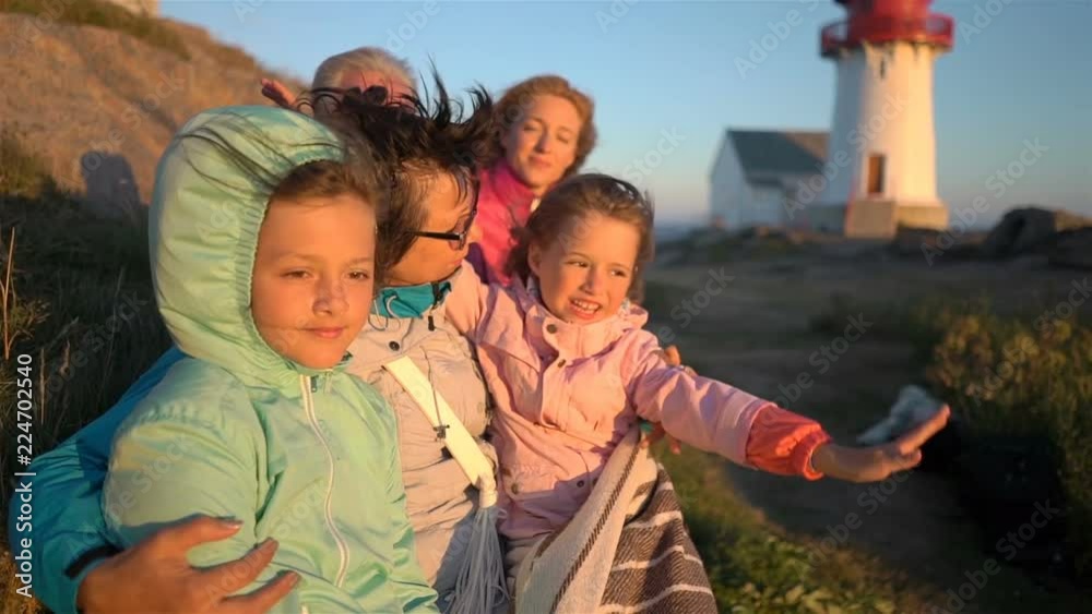 Big happy family admiring the sunset or sunrise on the rocky North shore of the sea with an old lighthouse Big happy family admiring the sunset or sunrise on the rocky North shore of the sea with an old lighthouse