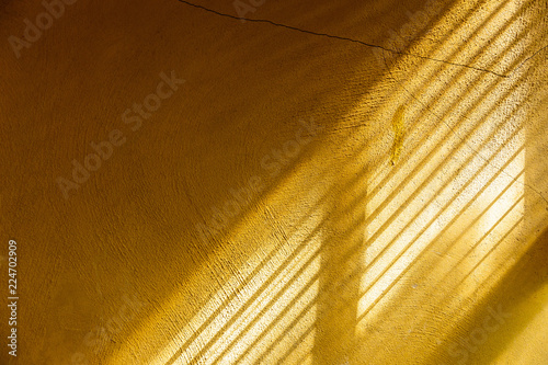 Yellow cement wall touching sunlight through window to show surface of rough wall and making separating parts of light and shadow.