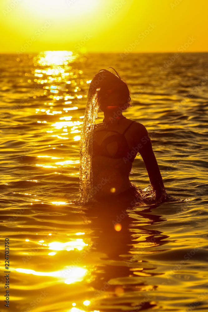Girl jumps out of the water with splashes at sunset