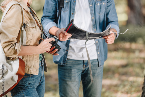 partial view of couple of tourists with photo camera and map in park