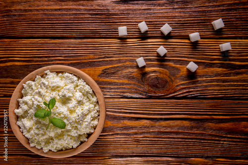 homemade cottage cheese in a wooden bowl, mint and sugar cubes lie on a wooden table