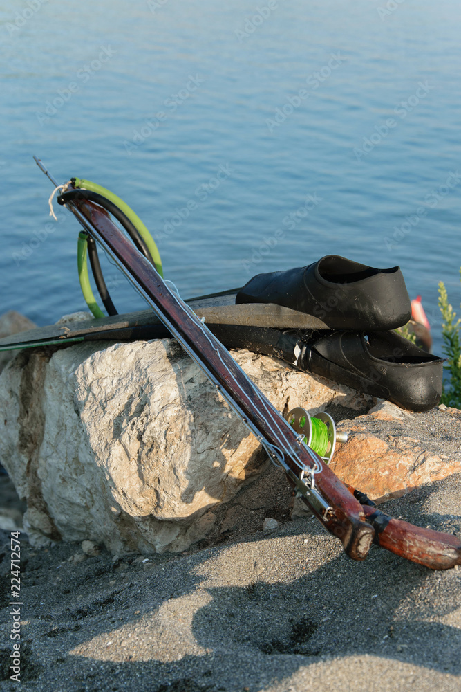 Spearfishing gear - fins, speargun on a sea rock against blue sea