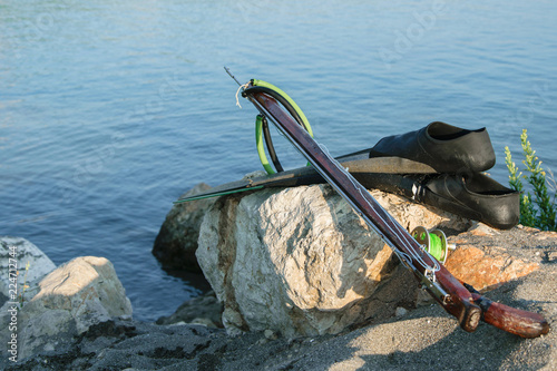 Spearfishing gear - fins, speargun  on a sea rock against blue sea background, space for text