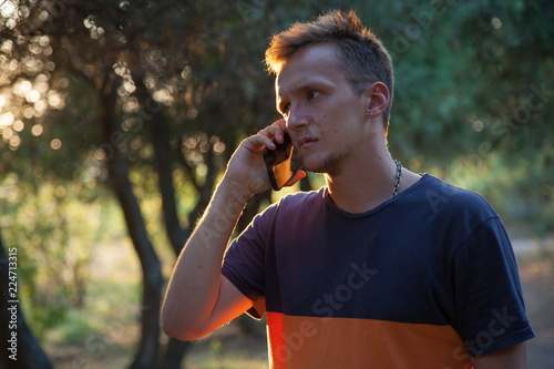 young serious man talking on the phone in the park at sunset 
