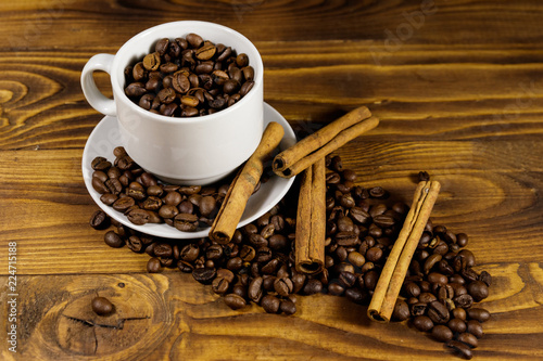 Coffee beans in white cup and cinnamon sticks on wooden table