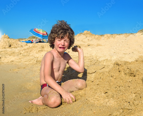 Crying boy on the beach. A small child sitting by the sea and hysterically crying photo