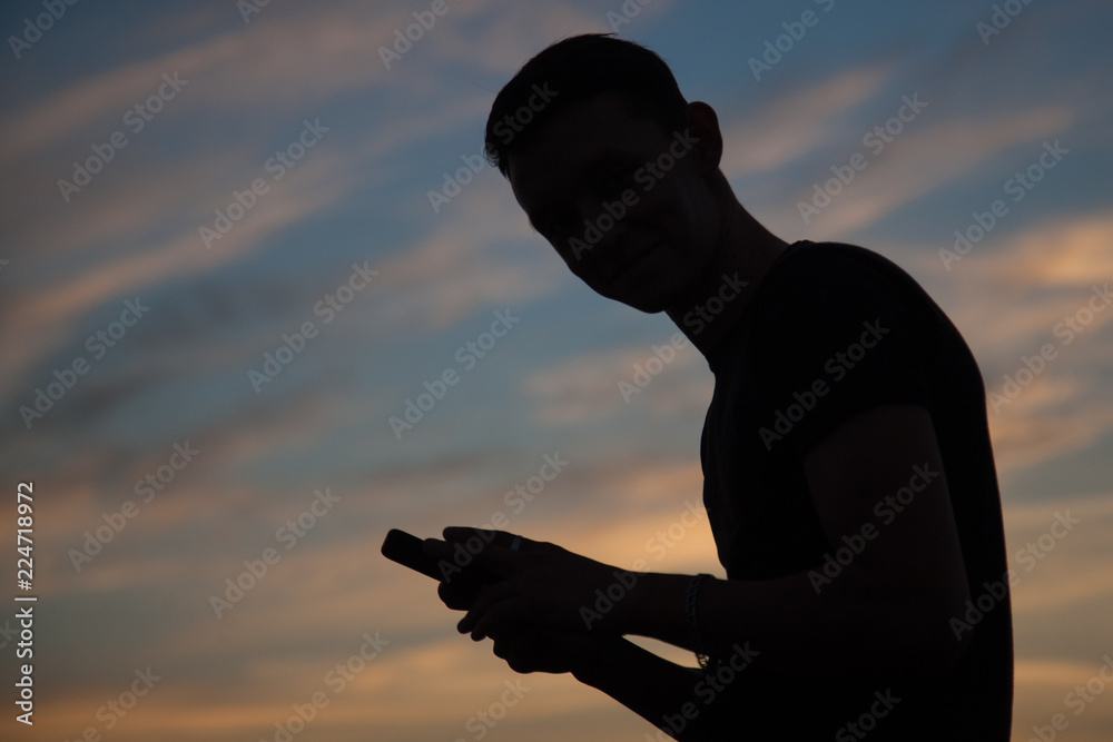 silhouette of young man with smartphone at sunset