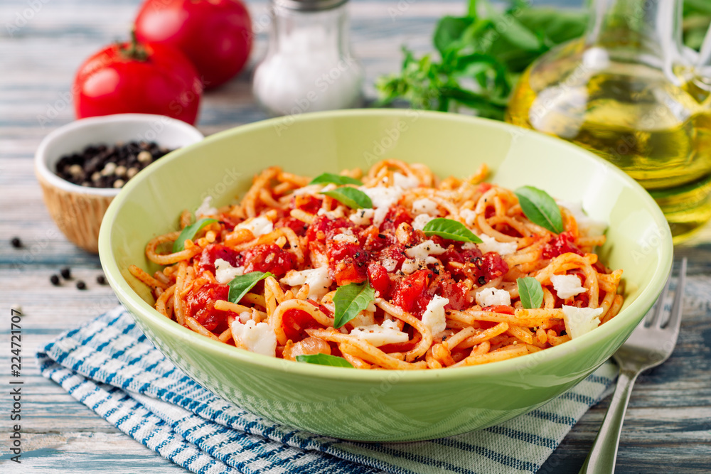Spaghetti pasta with tomato sauce, mozzarella cheese and fresh basil leaves on white-blue vintage wooden background. Selective focus. Spaghetti pasta with tomato sauce, mozzarella cheese and fresh basil leaves on white-blue vintage wooden background. Selective focus.