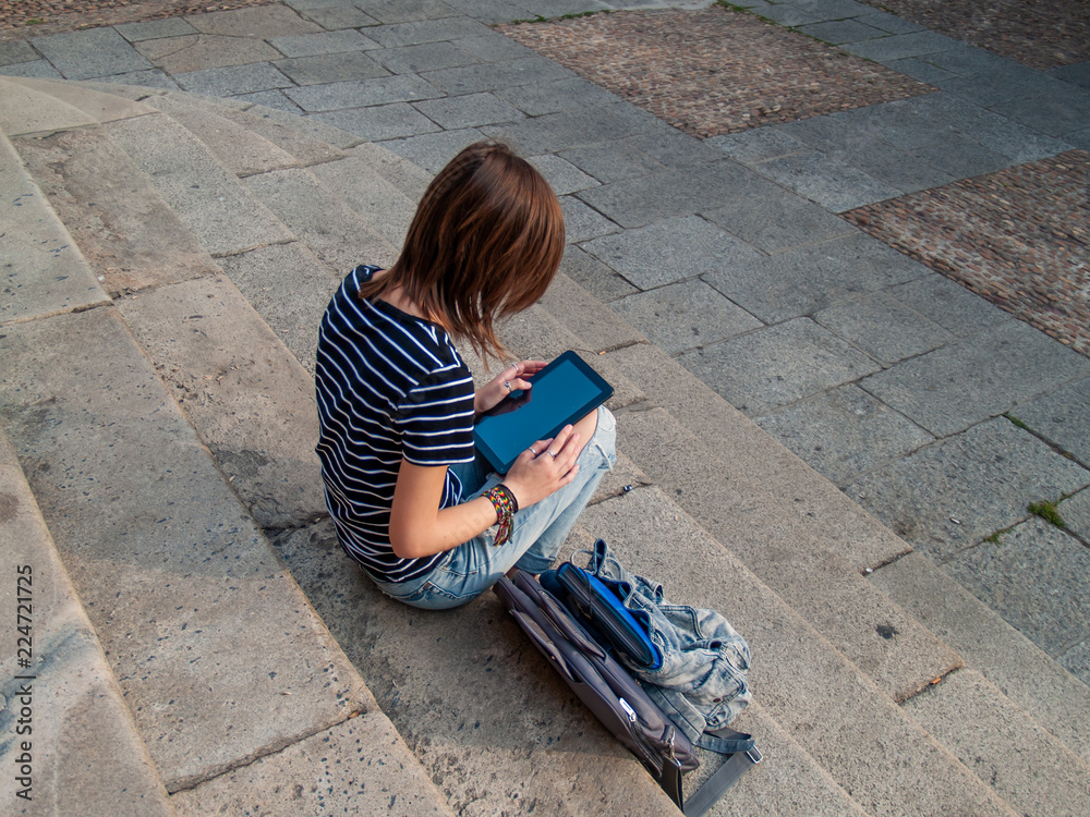A teenage woman with a tablet on the stairs of a university in a university campus A teenage woman with a tablet on the stairs of a university in a university campus