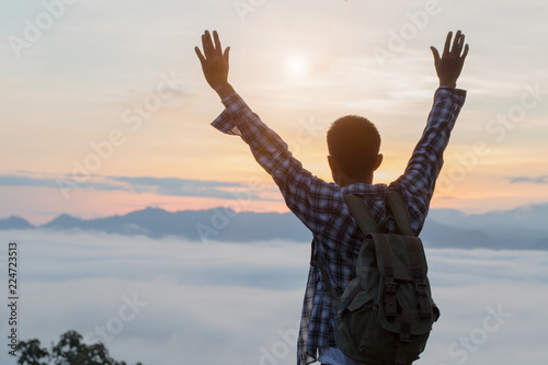 Tourist with backpack on  mountain slope with raised hands over  The valley is covered with  fog and has a beautiful sunrise. Beauty of nature  tourism and traveling concept.