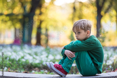 Caucasian boy worries because of problems. Sits one summer in the park alone and reflects