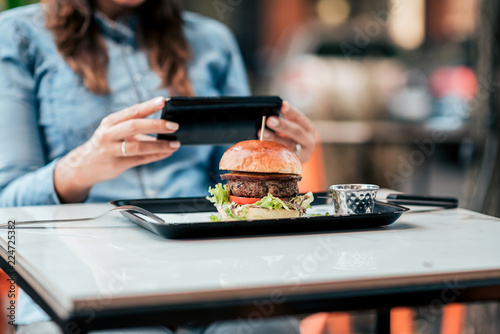 Woman taking a picture of food on her mobile phone in the restaurant. Close-up.