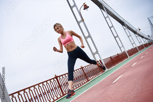 Morning workout. Close up of young womanin sports clothing exercising while jogging on the bridge outdoors