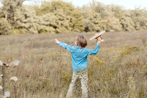 rear view of little kid in field playing with toy airplane in field