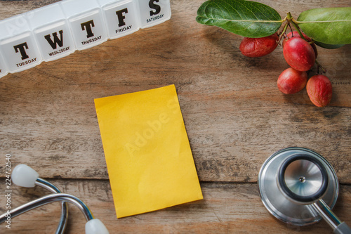 top view basic Health care concept with yellow note pad for copy space and Stethoscope,day pill box  and Bengal-Currants on the wooden table photo