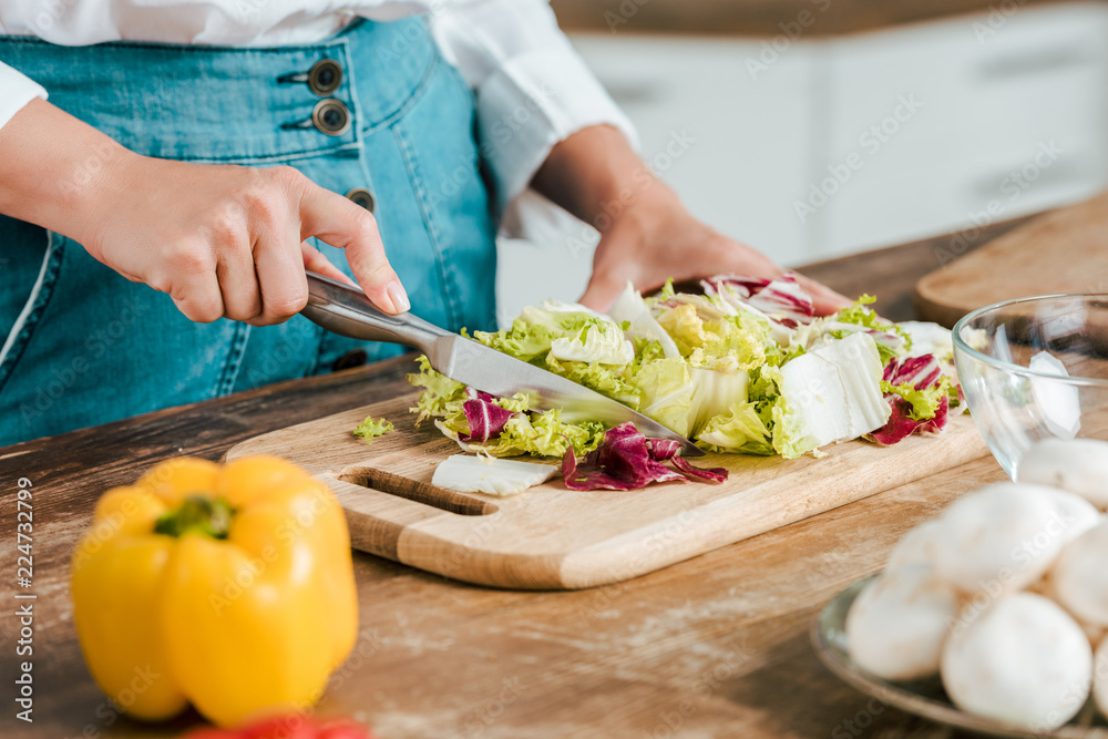 cropped shot of woman cutting lettuce for salad on wooden cutting board