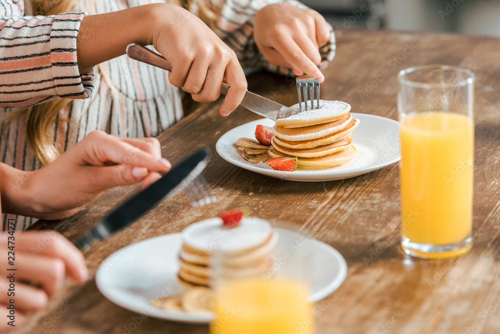 cropped shot of mother and daughter eating pancakes with strawberries