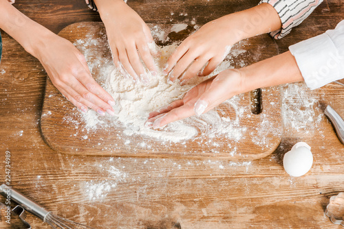 cropped shot of child and women making dough together on wooden board