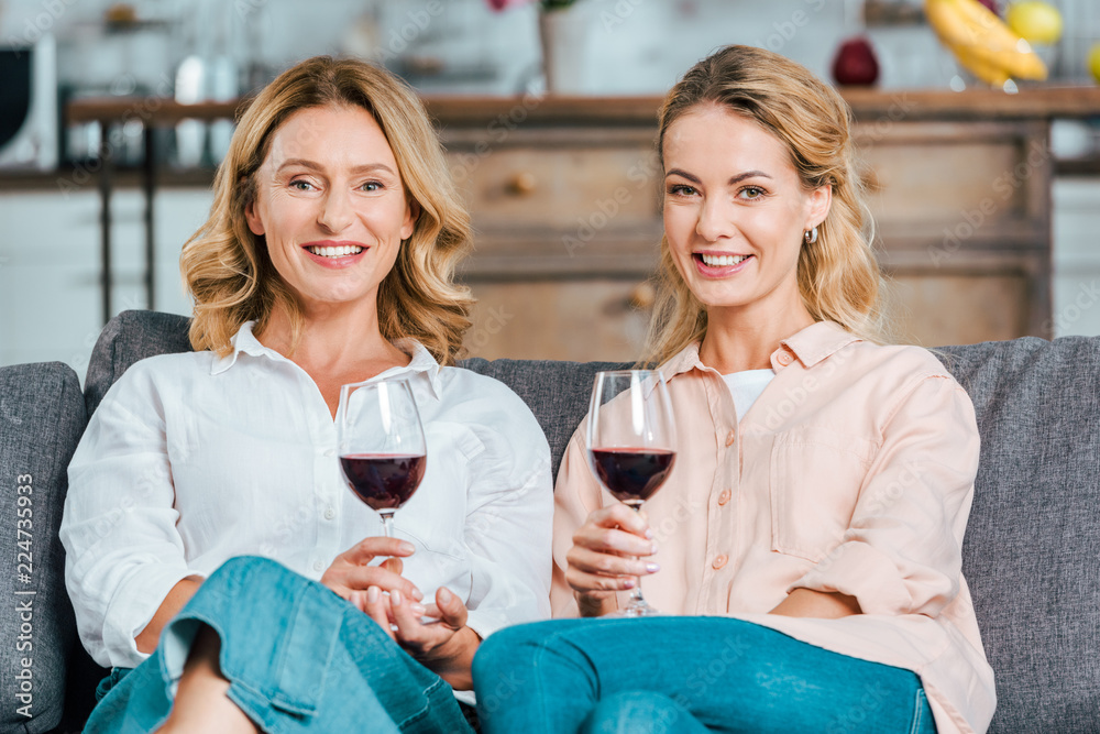 happy mature mother and adult daughter with glasses of red wine spending time together at home and looking at camera happy mature mother and adult daughter with glasses of red wine spending time together at home and looking at camera