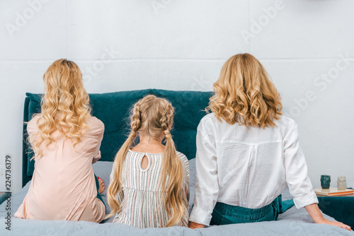 rear view of child with mother and grandmother sitting on bed at home