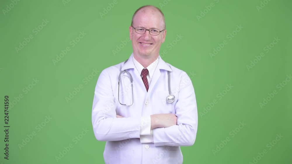 Happy mature bald man doctor with arms crossed against green background Happy mature bald man doctor with arms crossed against green background