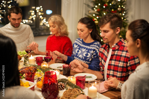 holidays and celebration concept - friends holding hands and praying while having christmas dinner at home