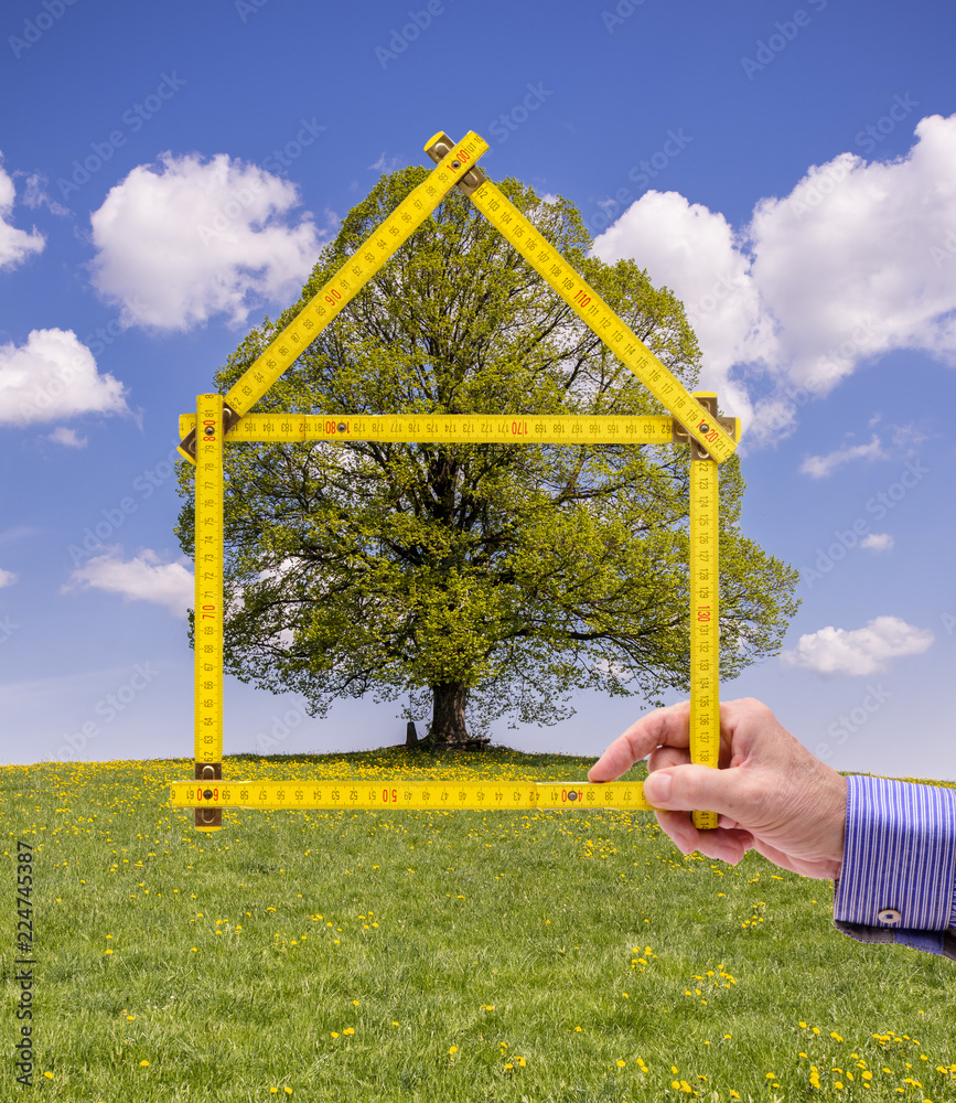 Makler hält Meterstab in Form von einem Haus als Symbol für Wohnen im Grünen Makler hält Meterstab in Form von einem Haus als Symbol für Wohnen im Grünen