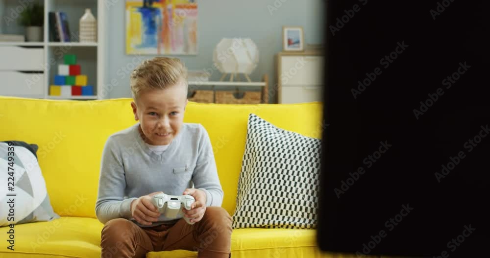 Small nice teen boy playing a videogame while sitting on the couch in the living room and winning.