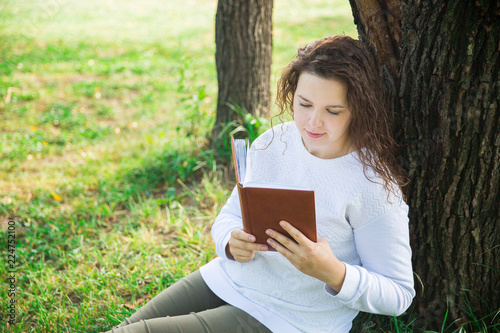 Girl in white with brown book in the park. Reading in the forest