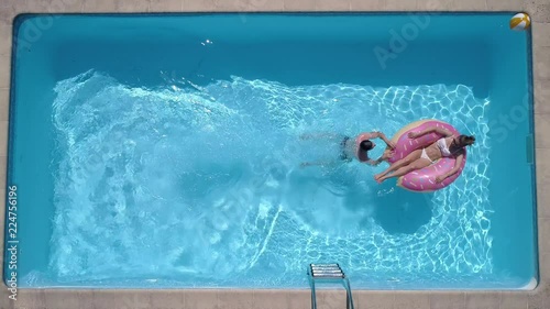 Aerial - Adult man dives into the the pool while girl is lying on a pool float