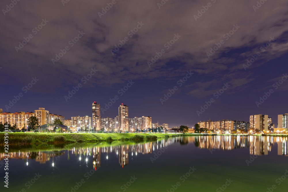 Night cityscape of residential buildings and park with a pond in the urban outskirts