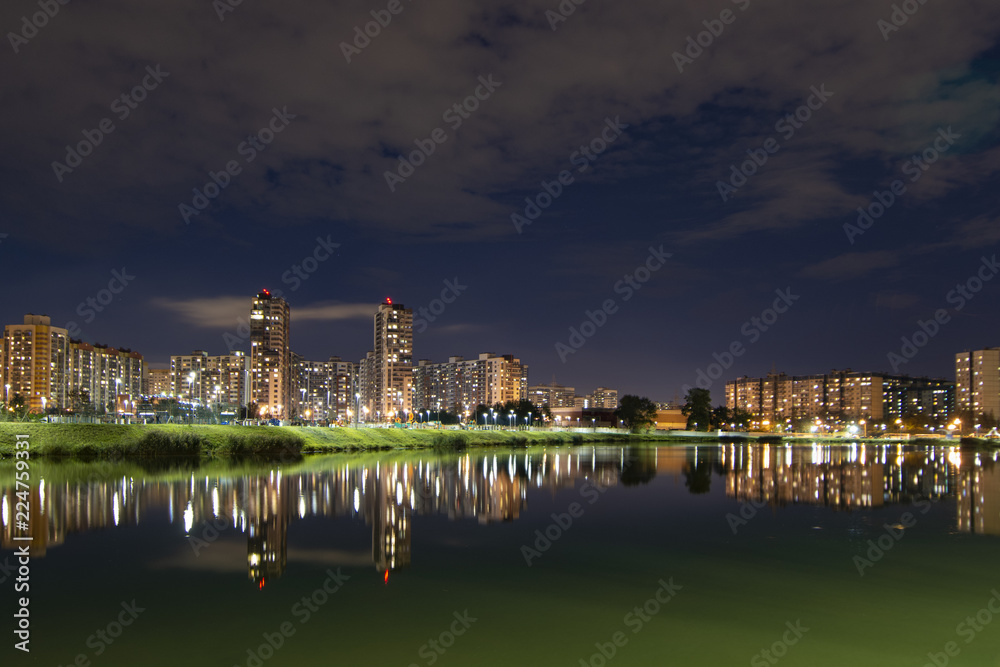 Night cityscape of residential buildings and park with a pond in the urban outskirts