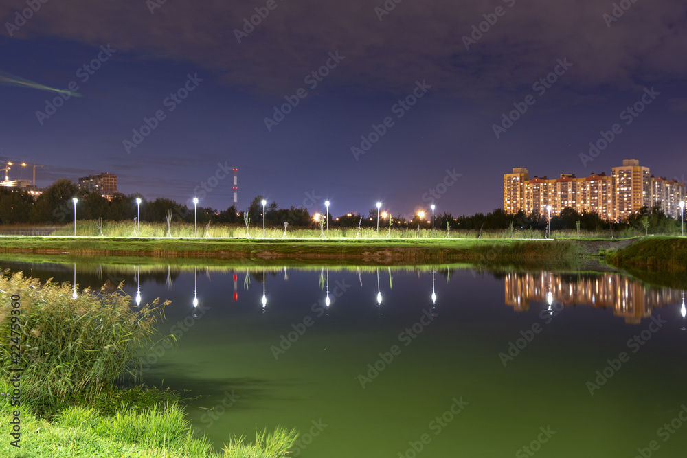 Night cityscape of residential buildings and park with a pond in the urban outskirts