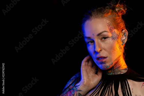 Muscled caucasian woman with tattoos and oiled skin wearing necklace and fishnet underwear poses under colored lights