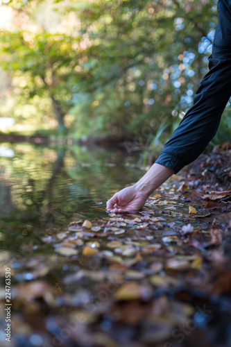 Male hand in a natural lake with autumn leaves.