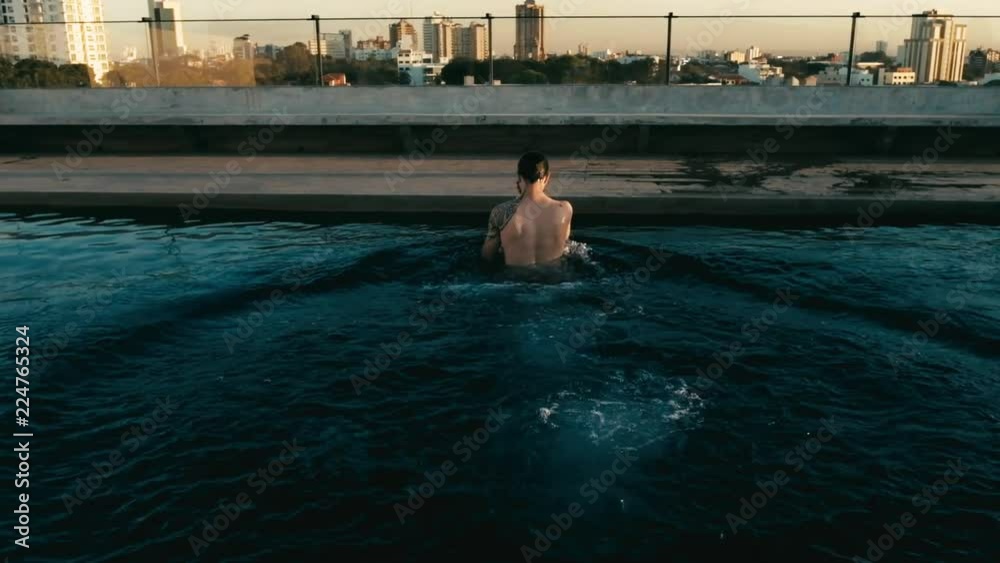 young man jumping to the rooftop pool above the city young man jumping to the rooftop pool above the city