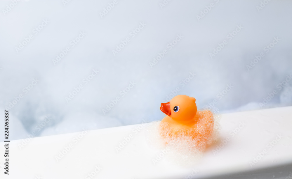 Orange playful rubber duck in a bubble bath, light blue background with bubbles. Kids spa concept. Children`s bath time concept. - obrazy, fototapety, plakaty 