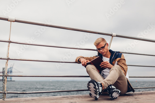 College student with backpack reading book by sea on pier in Odessa on rainy autumn day photo